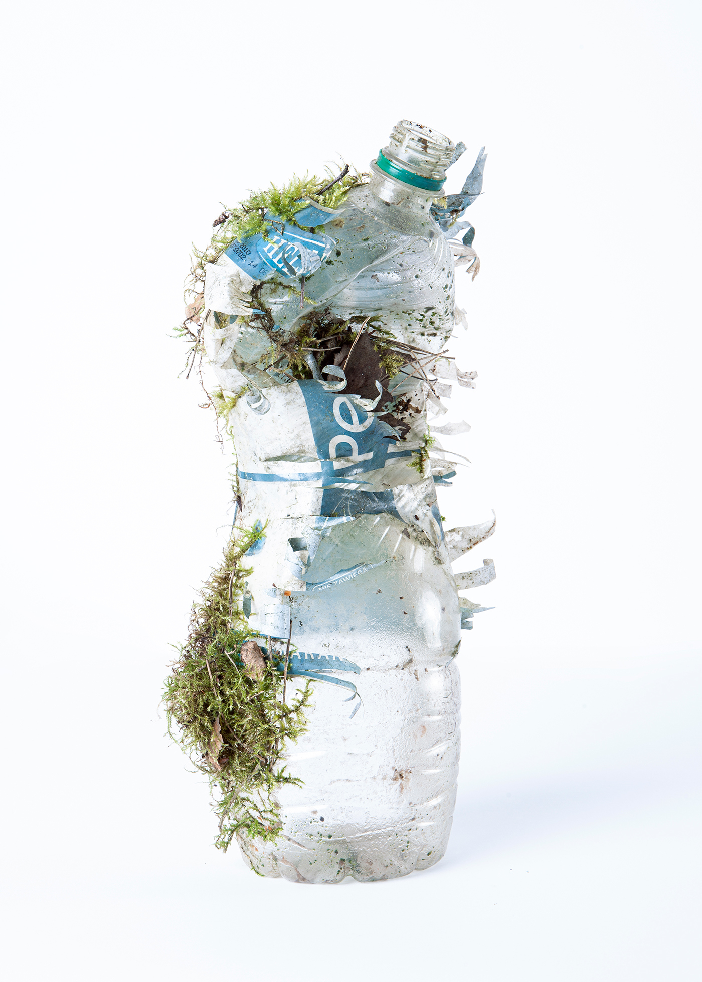 Zgnieciona plastikowa butelka pokryta ziemią i roślinnością.